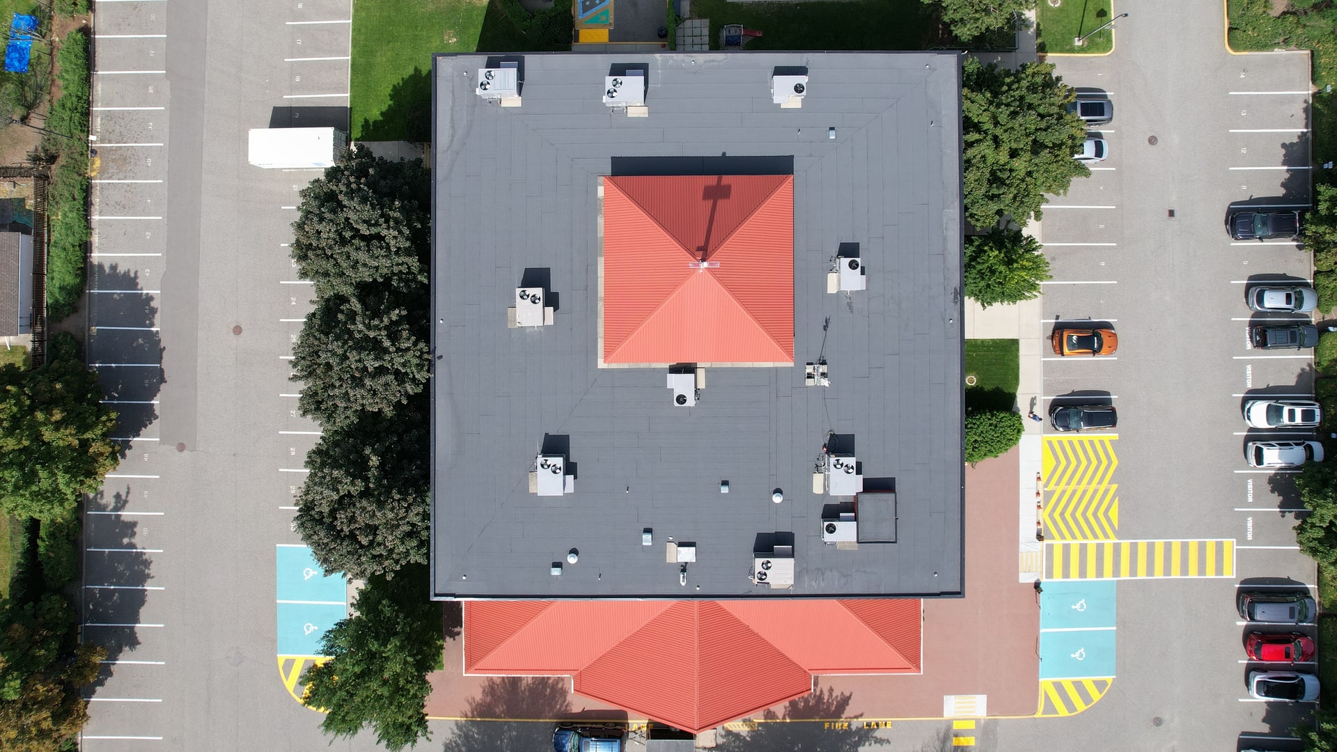 The same flat roof from straight above in August 2025, finished in black torch-on membrane around the red metal roofs