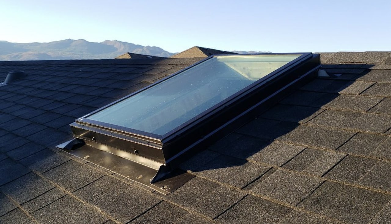 Skylight with black flashing on a shingle roof in low sun, mountains behind