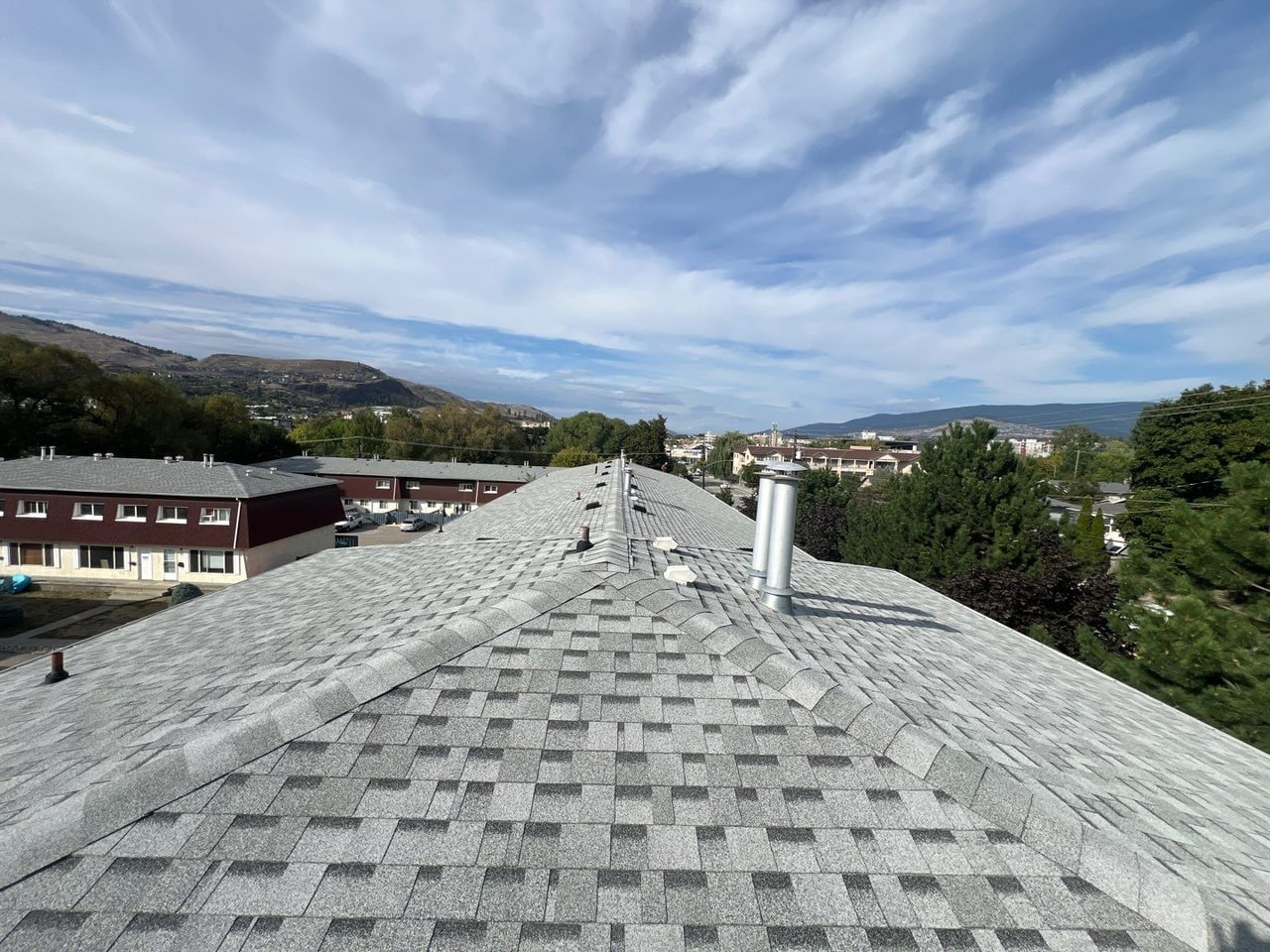 New light-grey architectural shingles along a multi-unit building, the Vernon hills and sky beyond