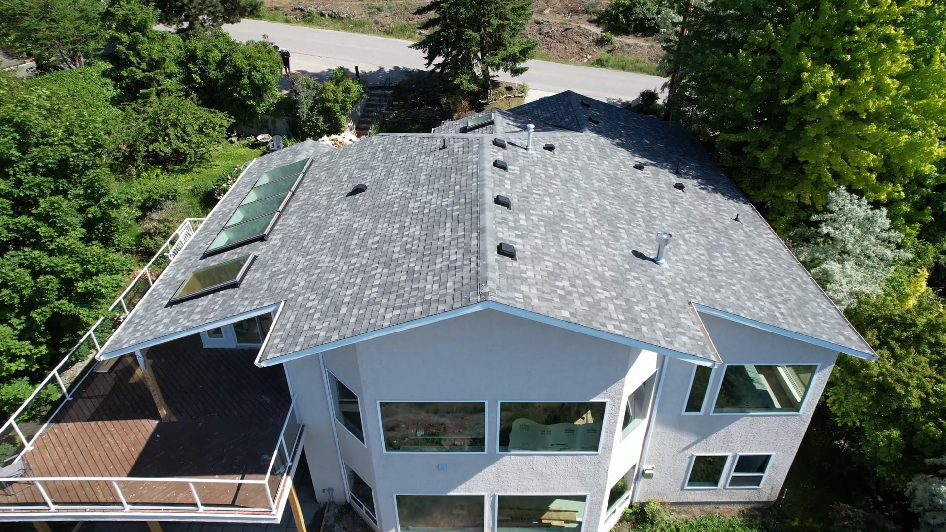 A finished architectural shingle roof with skylights on a white hillside home